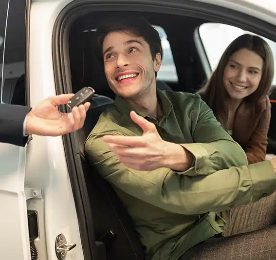 Couple taking car key sitting inside modern automobile at dealership