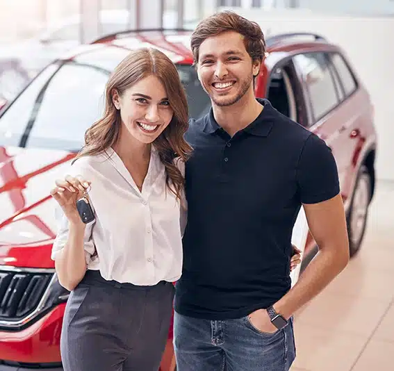 Cheerful man and woman smiling and showing keys while standing near vehicle