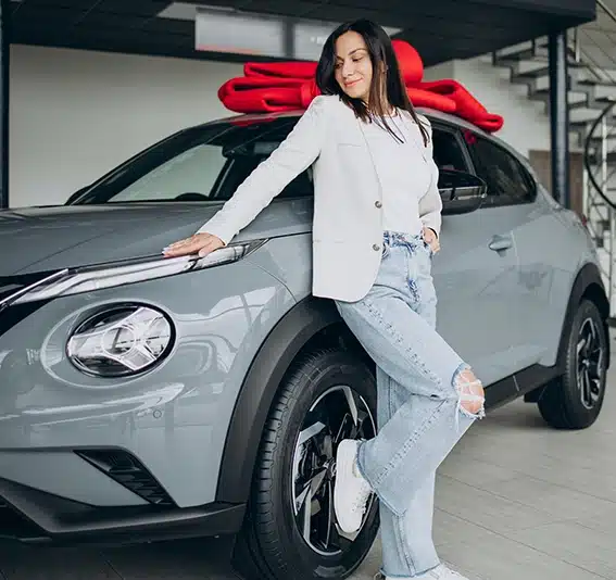 Woman in car showroom standing by her new car with red bow