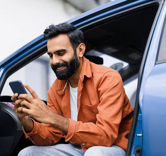Man sitting in his open car, calculating cheap rates for new car repayments with Jade Finance easy car calculator on his phone.