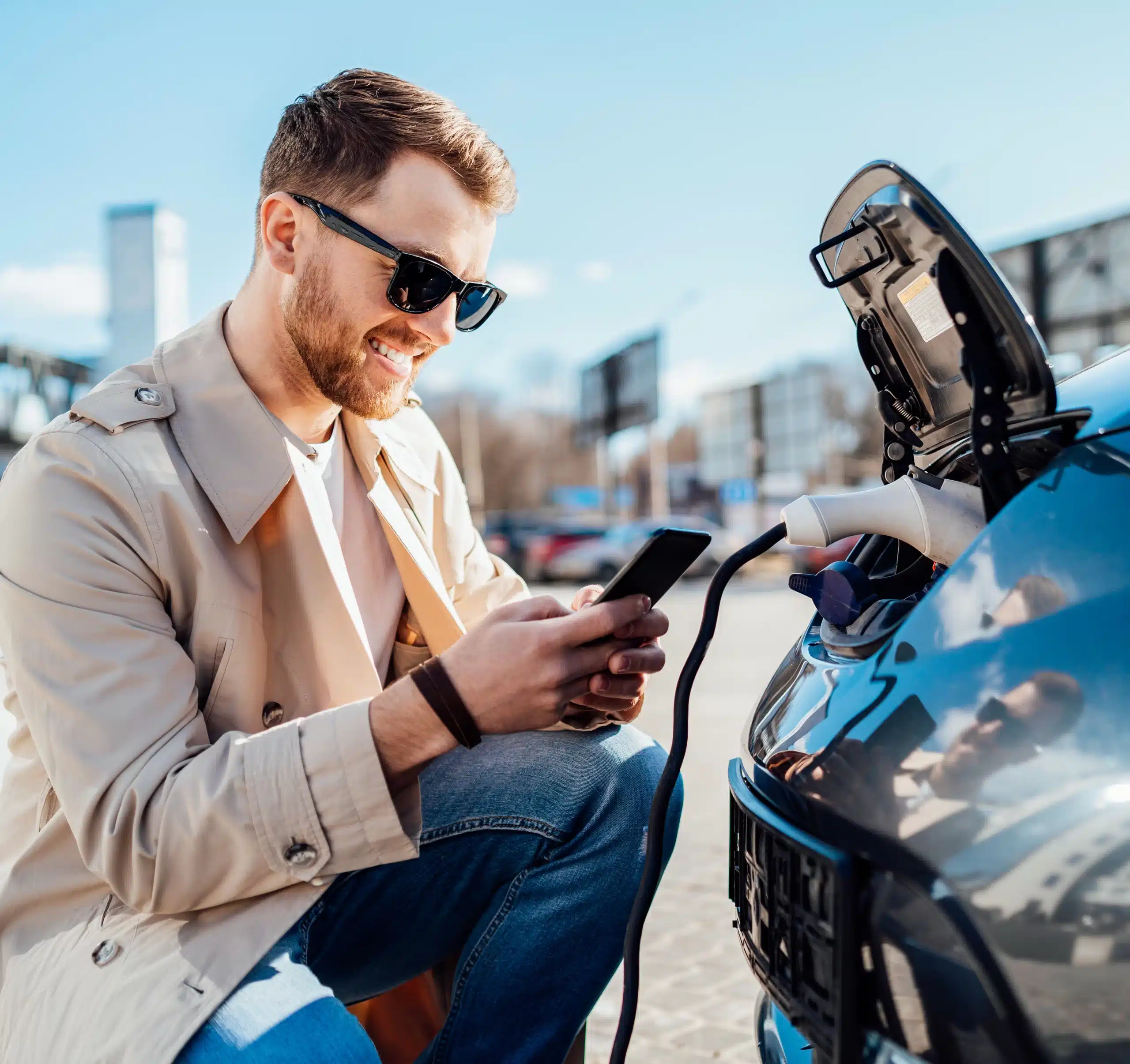 Casual man with smartphone near electric car