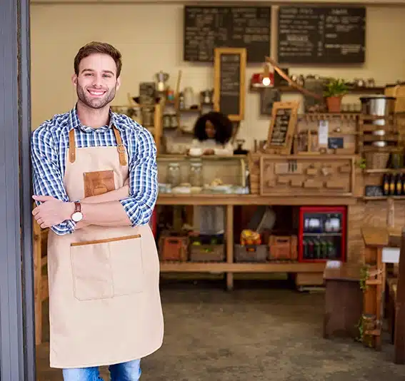 A smiling young man standing with his arms crossed while leaning on the door of a trendy cafe