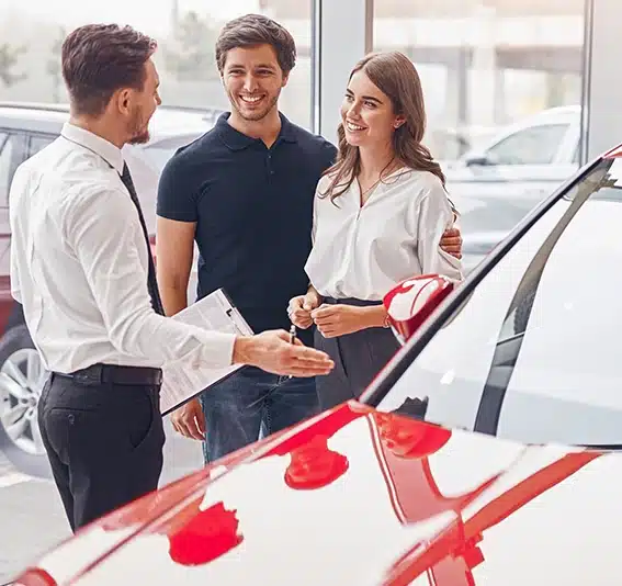 Young woman and man chatting with dealer while picking new red car