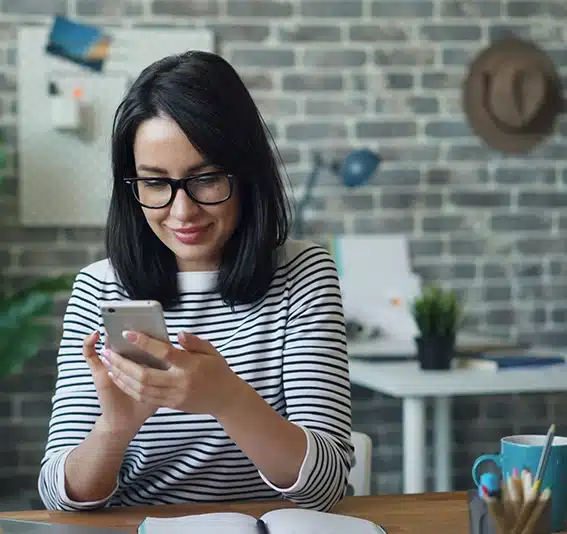 A woman with glasses sitting on a table looking at her cellphone