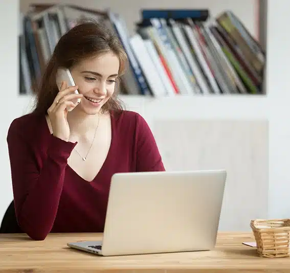 A smiling woman talking on phone looking at computer screen