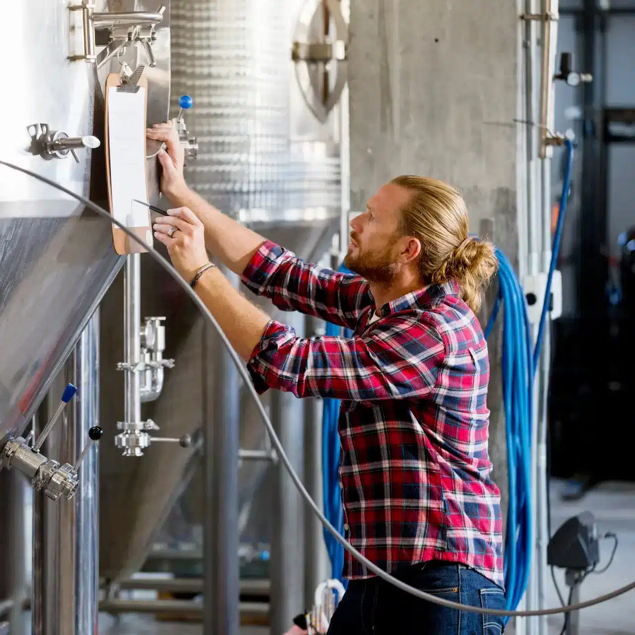 A man checks off items on his list of processes while monitoring this brewing equipment