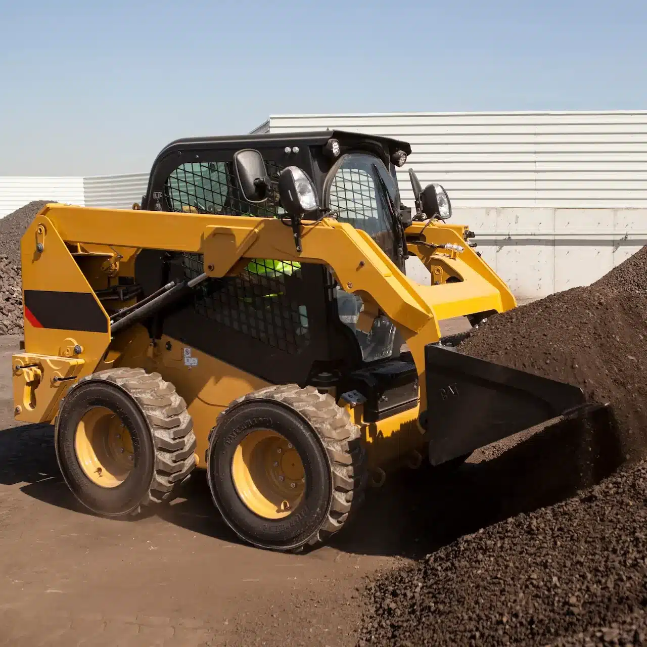A skidsteer bobcat is loading up it's front bucket with soil from a pile on the ground to move it to another place