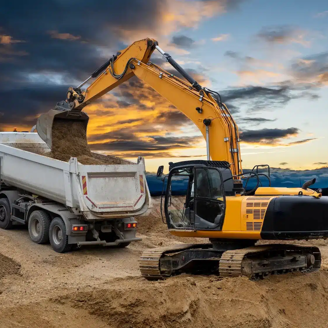 An excavator lowers a bucket load of dirt into a tipper truck on a construction site