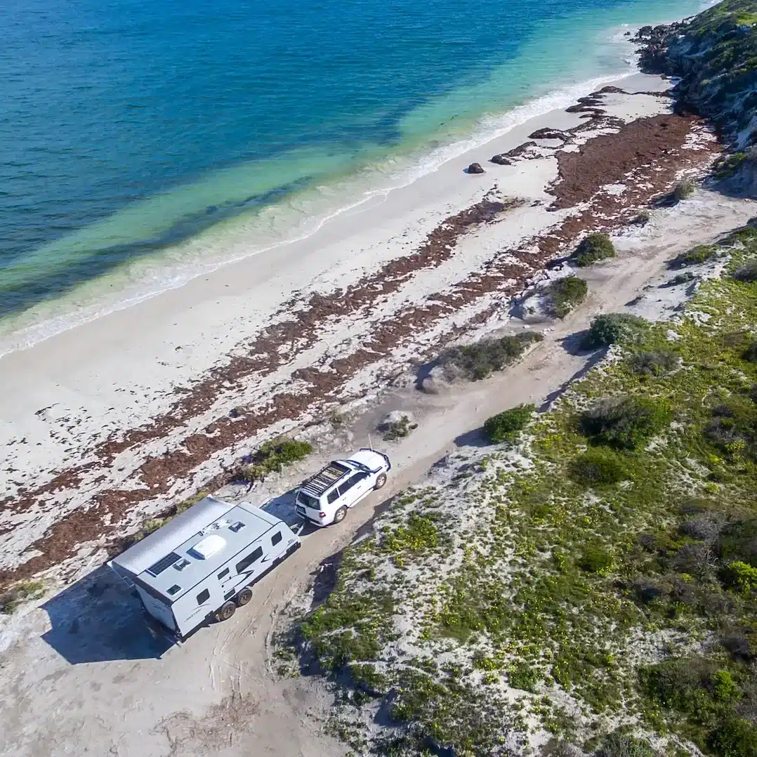 Aerial view of caravan and 4WD on a beach track right next to the ocean