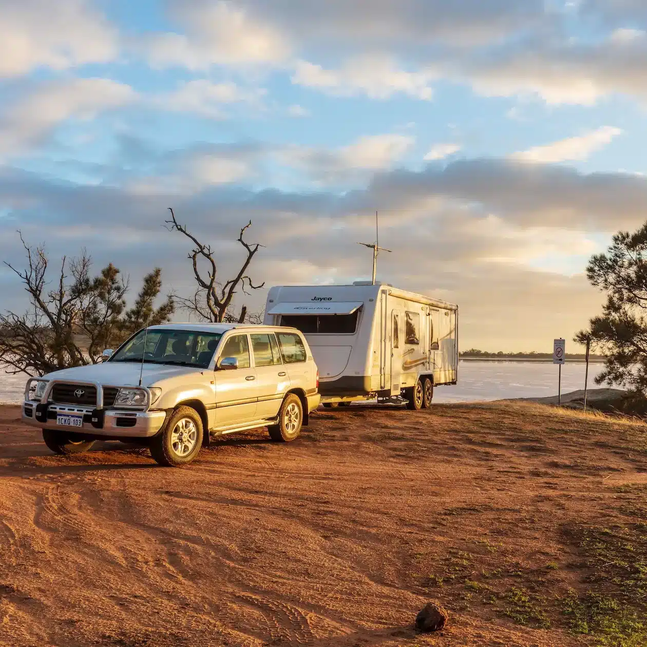 A used caravan hooked up to a 4WD parked next to a lake at sunset