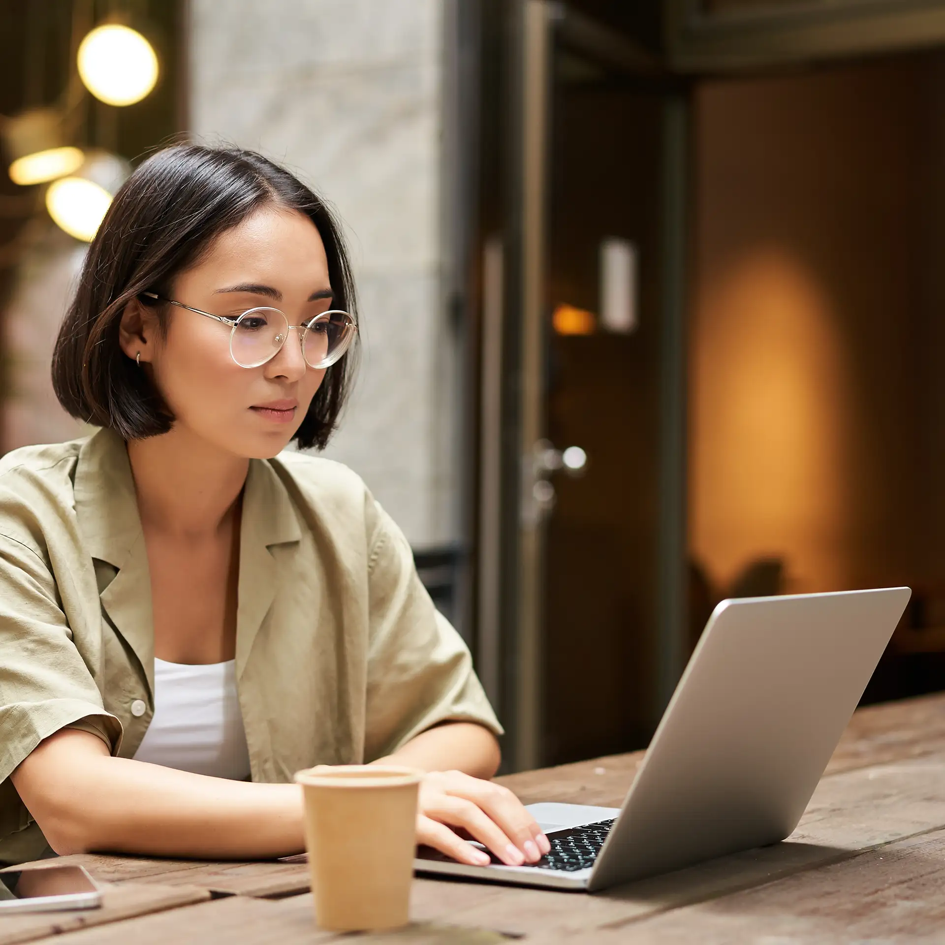 Young woman working in a cafe, using laptop and drinking coffee