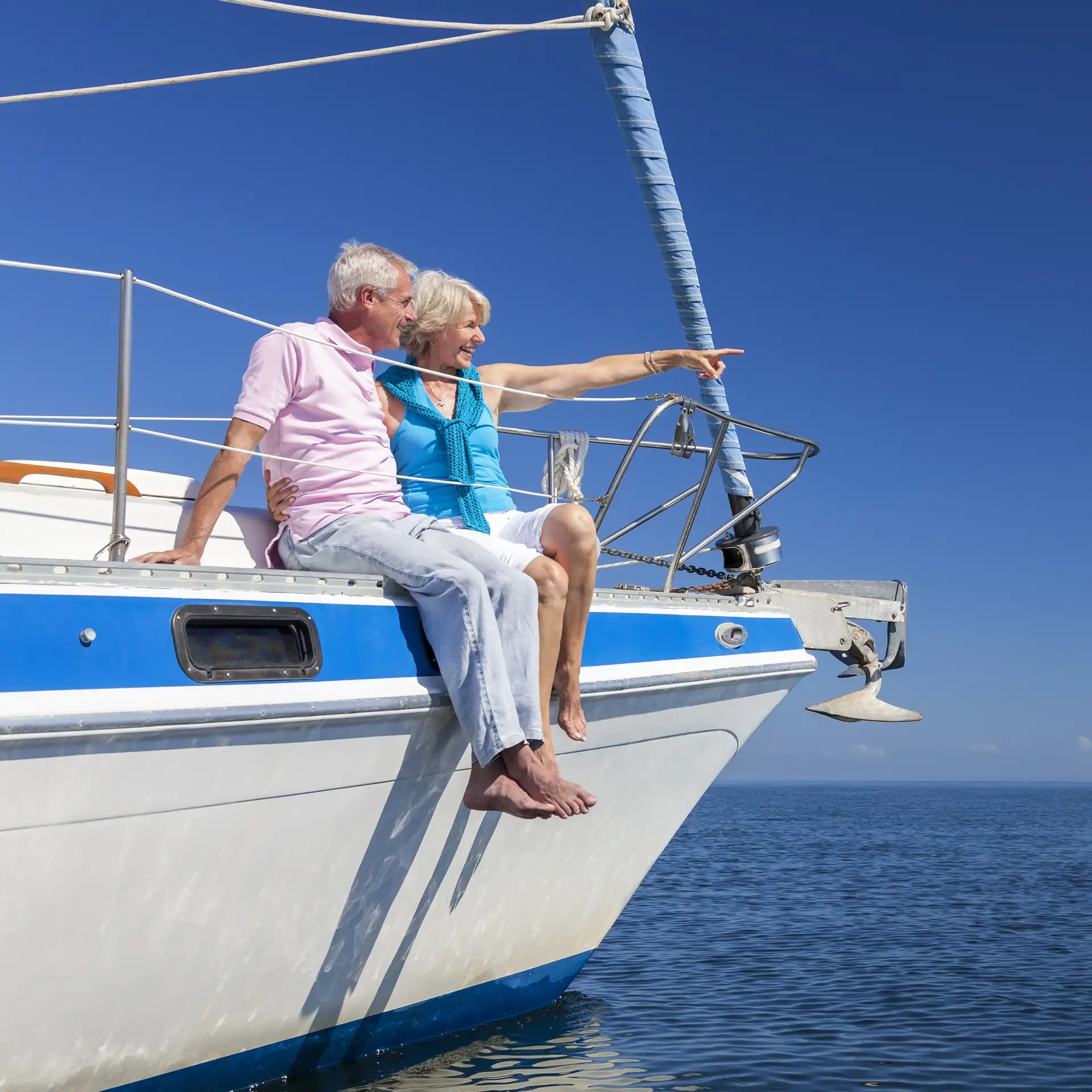 A happy senior couple sitting on the side of a sail boat pointing to a clear horizon