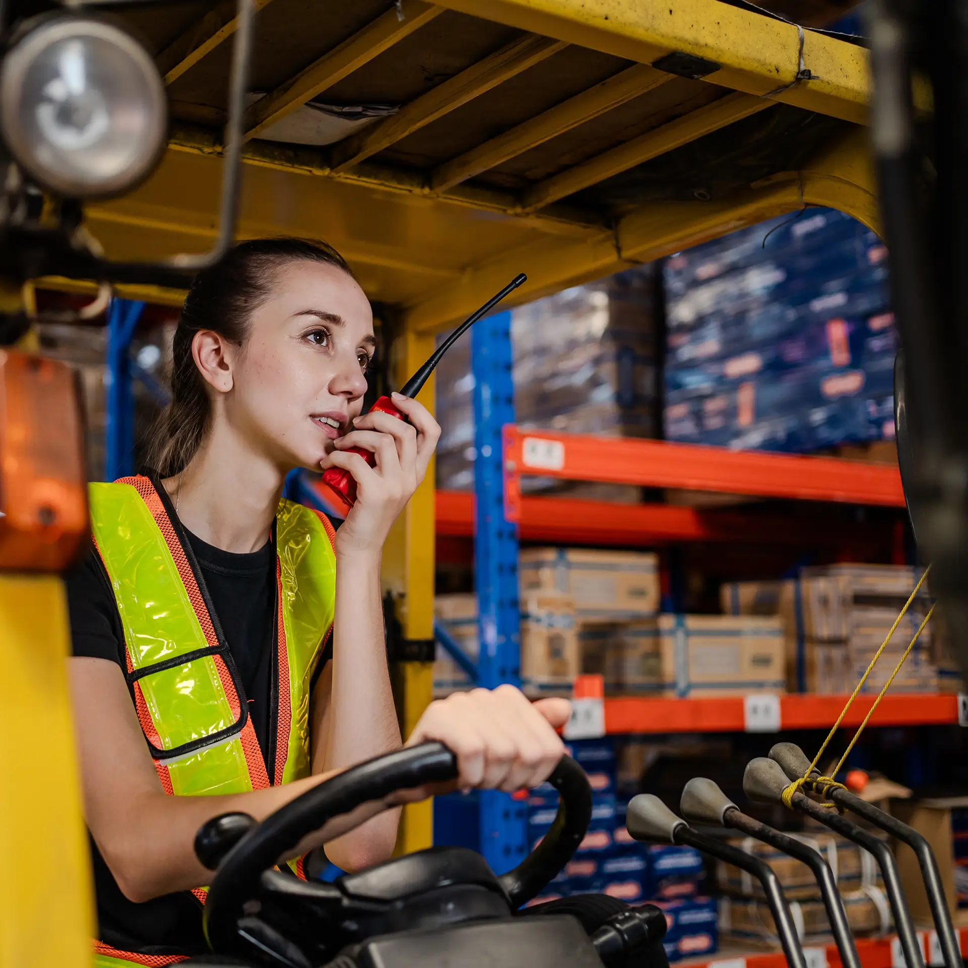 A woman in a yellow safety vest is driving a forklift