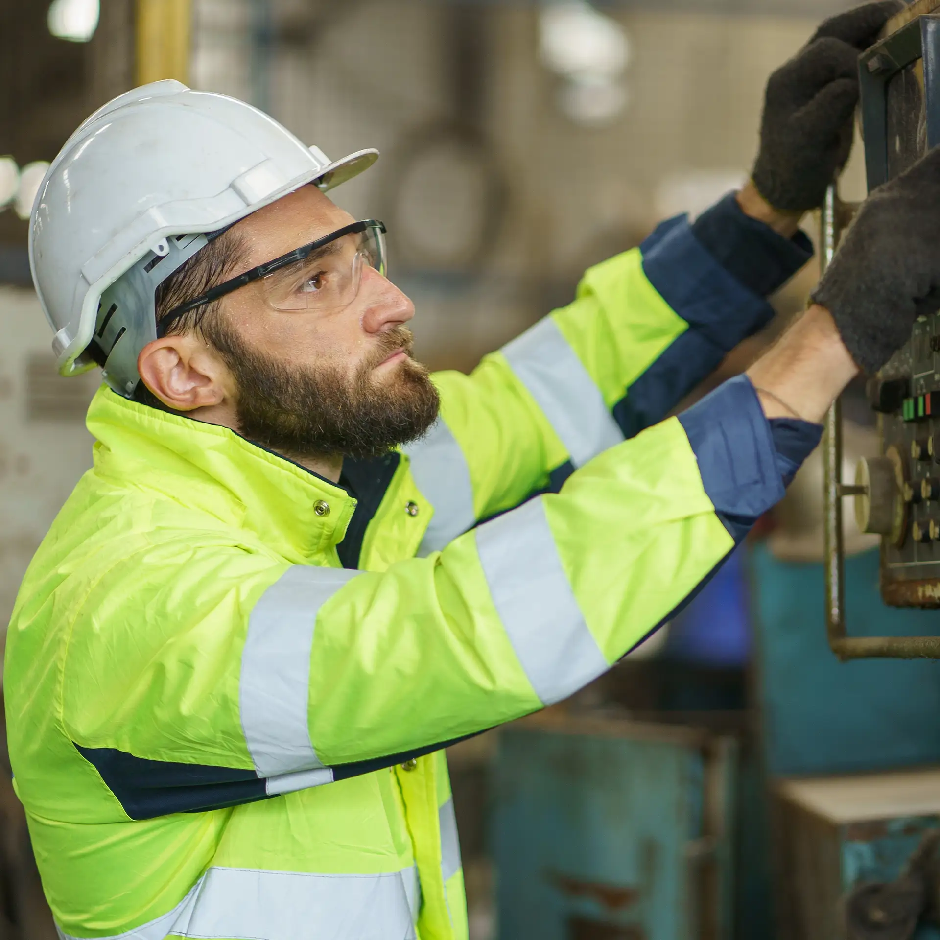 Caucasian industrial worker with a beard, wearing a helmet, controlling a CNC machine in an industrial factory