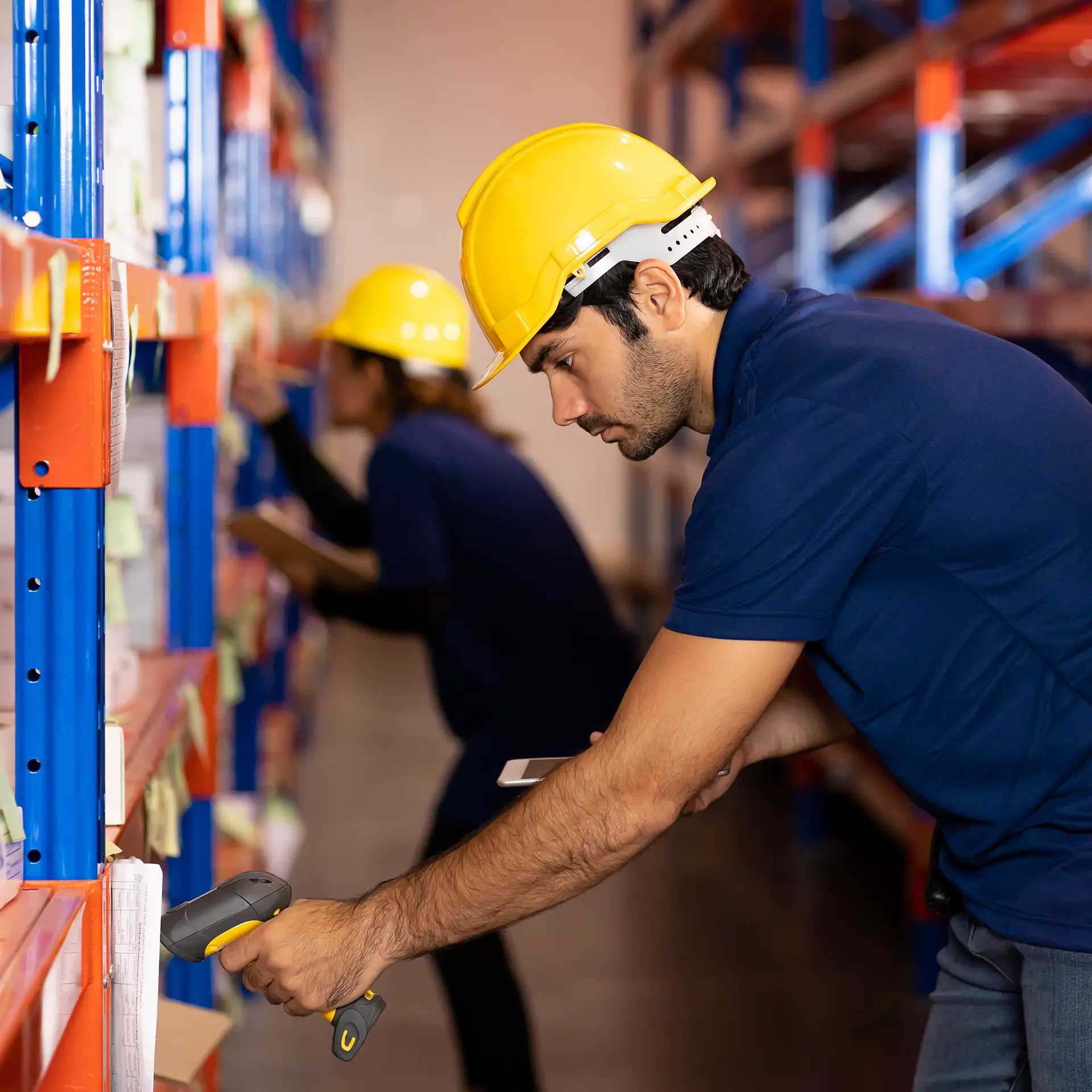 A male warehouse worker using a barcode scanner to check products or parcels on pallets in an industrial warehouse