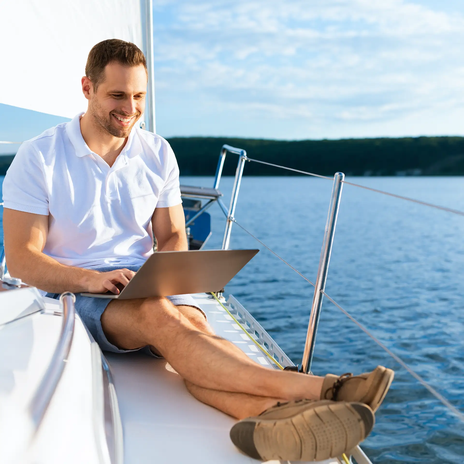 Man smiling while sitting with a laptop on a sailboat, getting a best low rate loan with Jade Finance.