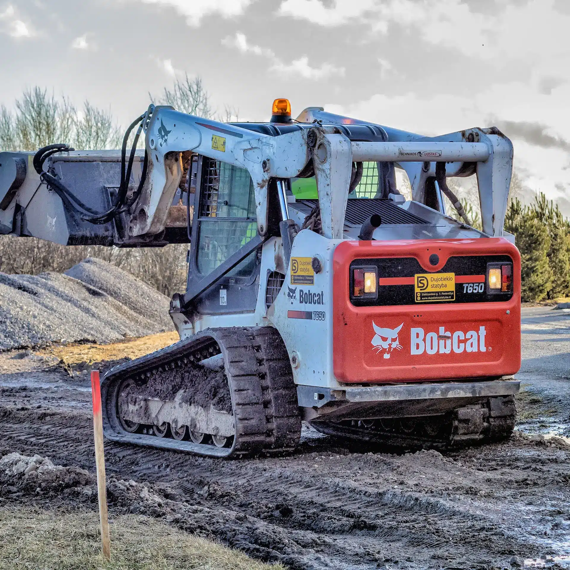 A Bobcat on tracks moving ground rock and levelling it across the ground.