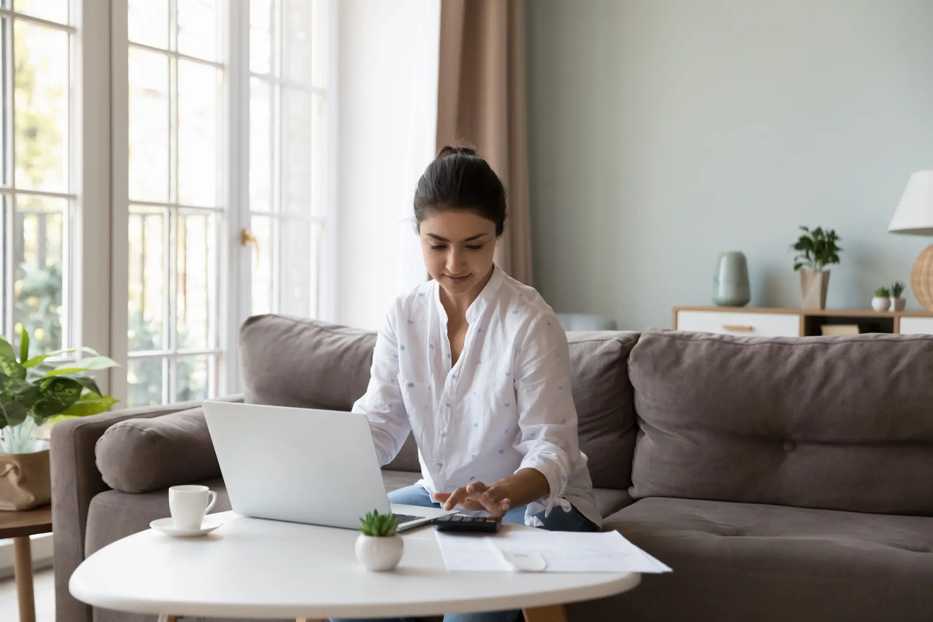 A young woman is calculating her balloon payment at her coffee table with laptop and papers.