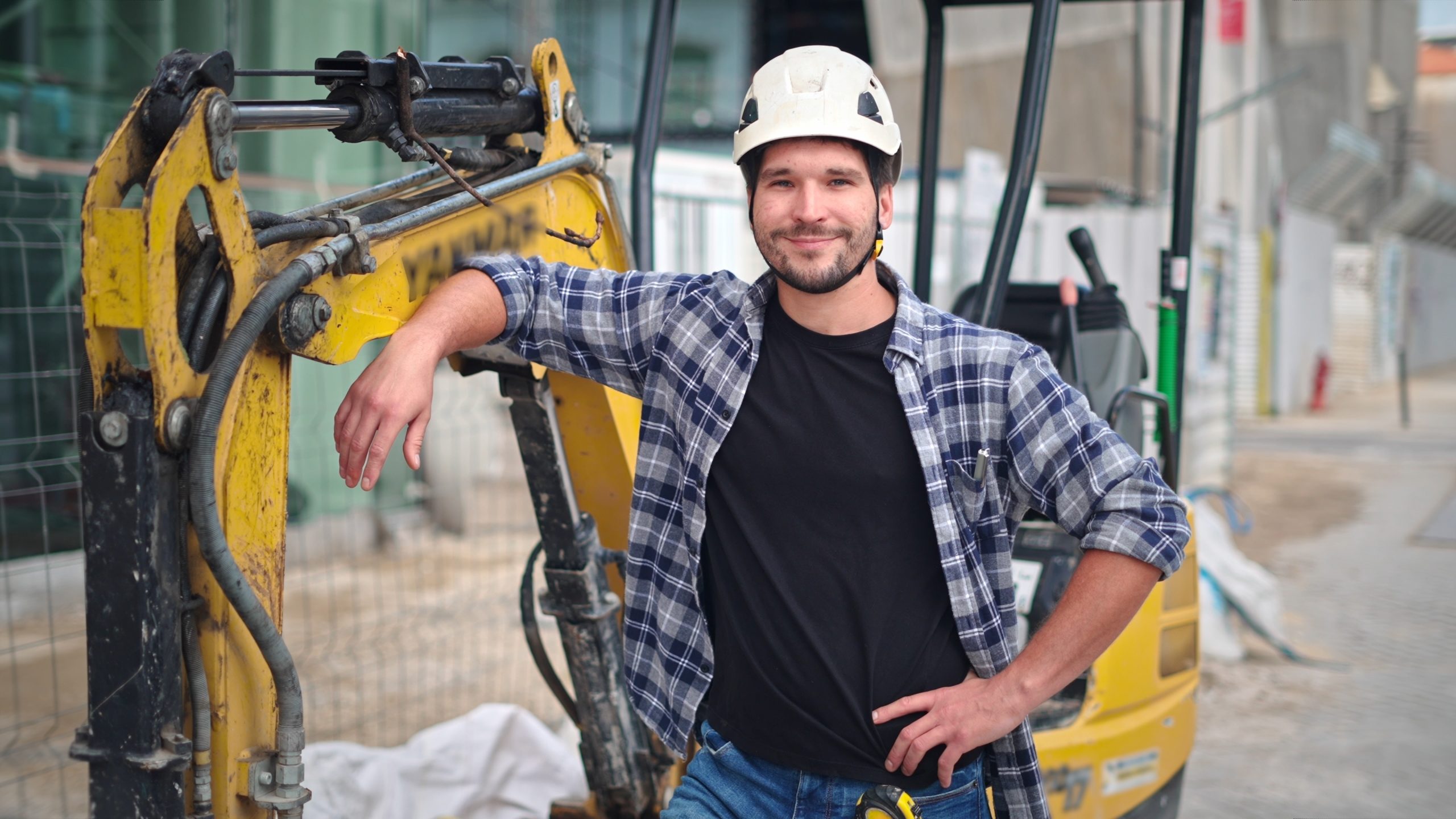 A smiling construction worker leans on his digger on a construction site.