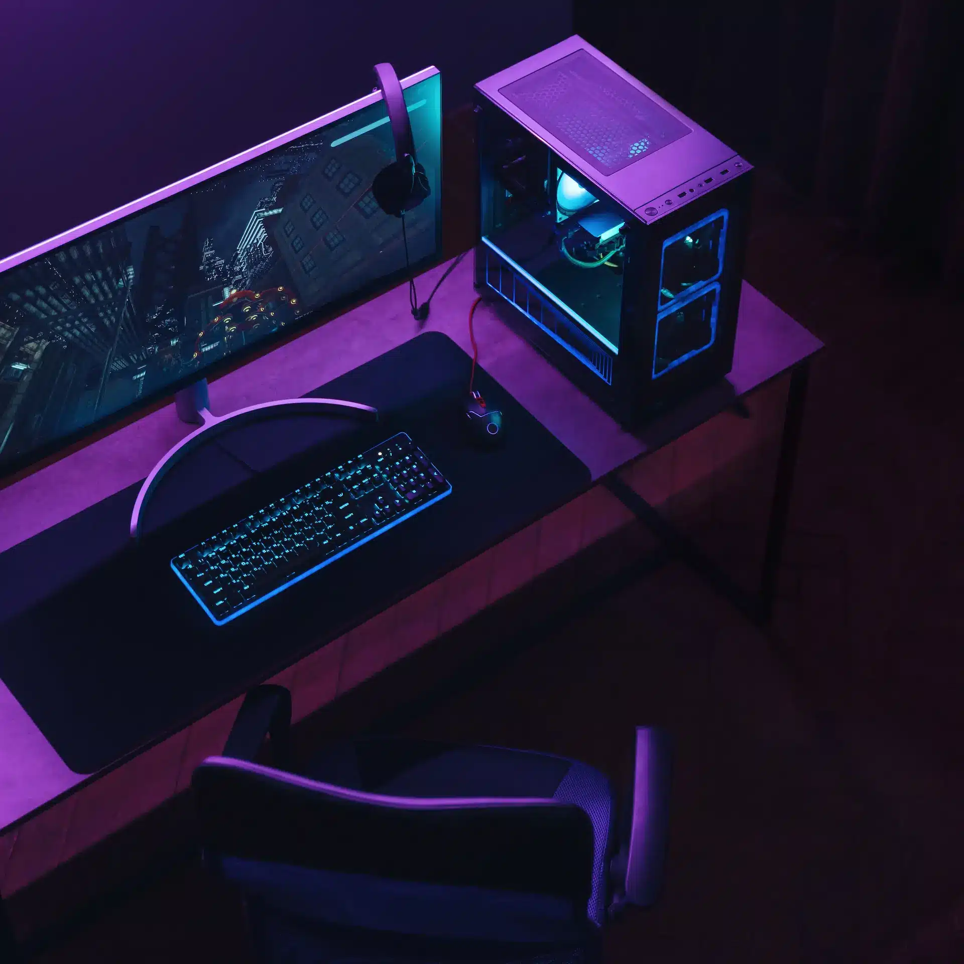 View of a gaming computer setup on a desk in a dark room lit with purple mood lighting, top down view, computer running with LED lighting.
