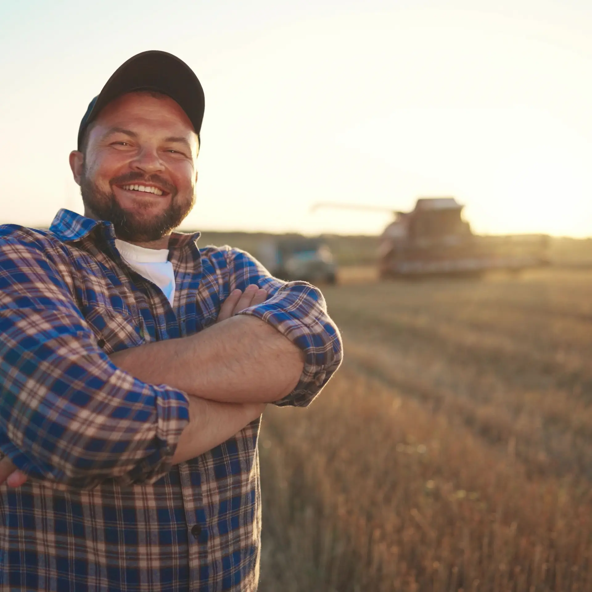 A proud farmer sanding in his field near sunset with his harvesting equipment in the background, happy that he chose to finance his new equipment to leverage his operational cash flow.