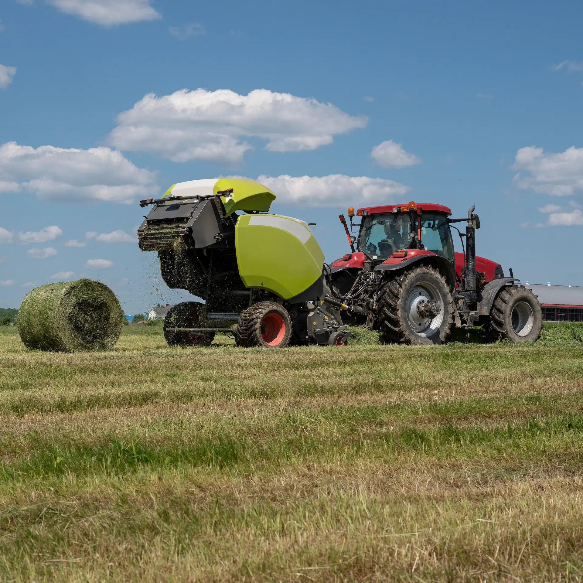 A hay bailing machine pulled behind a tractor creating large rolls of hay ready for collection and storage.