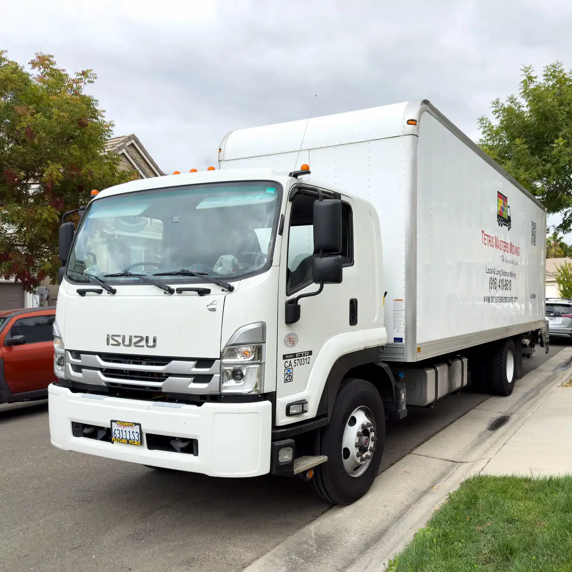 A white Isuzu truck with white rigid body parked kerbside.