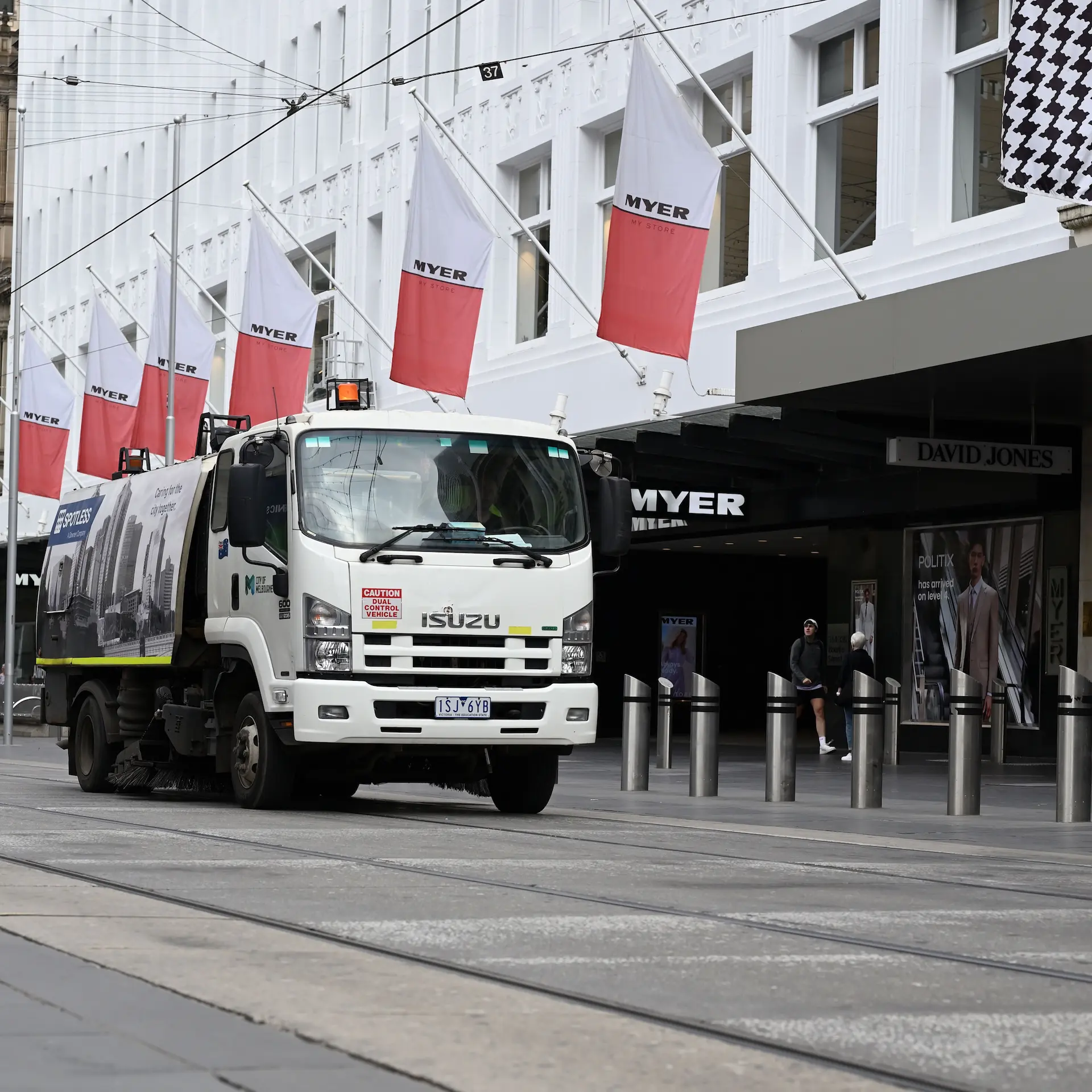 A white Isuzu waste collection truck driving down a main road in Melbourne.