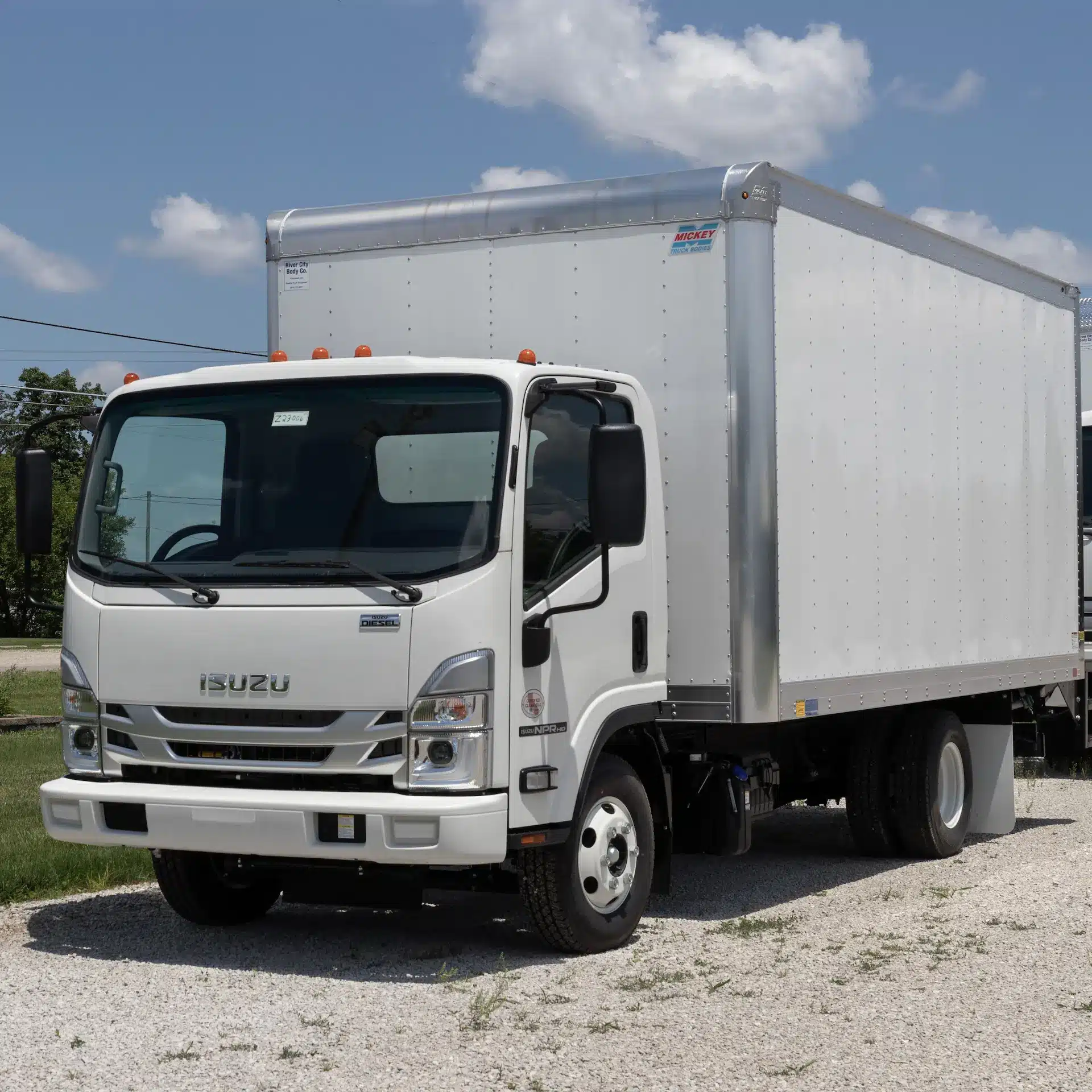 A white Isuzu truck with white rigid body parked at a truck stop.