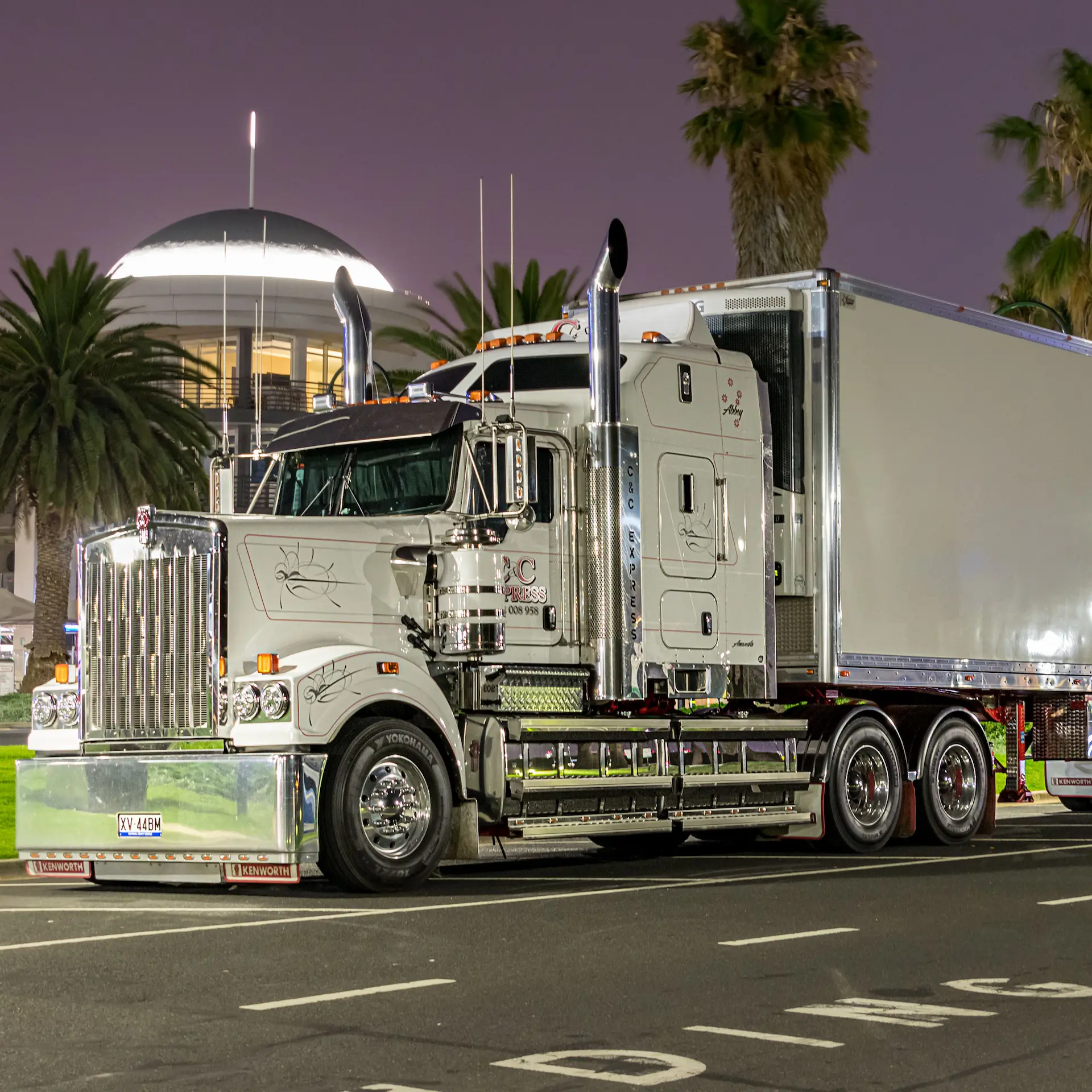 A white Kenworth big rig parked in town at night.