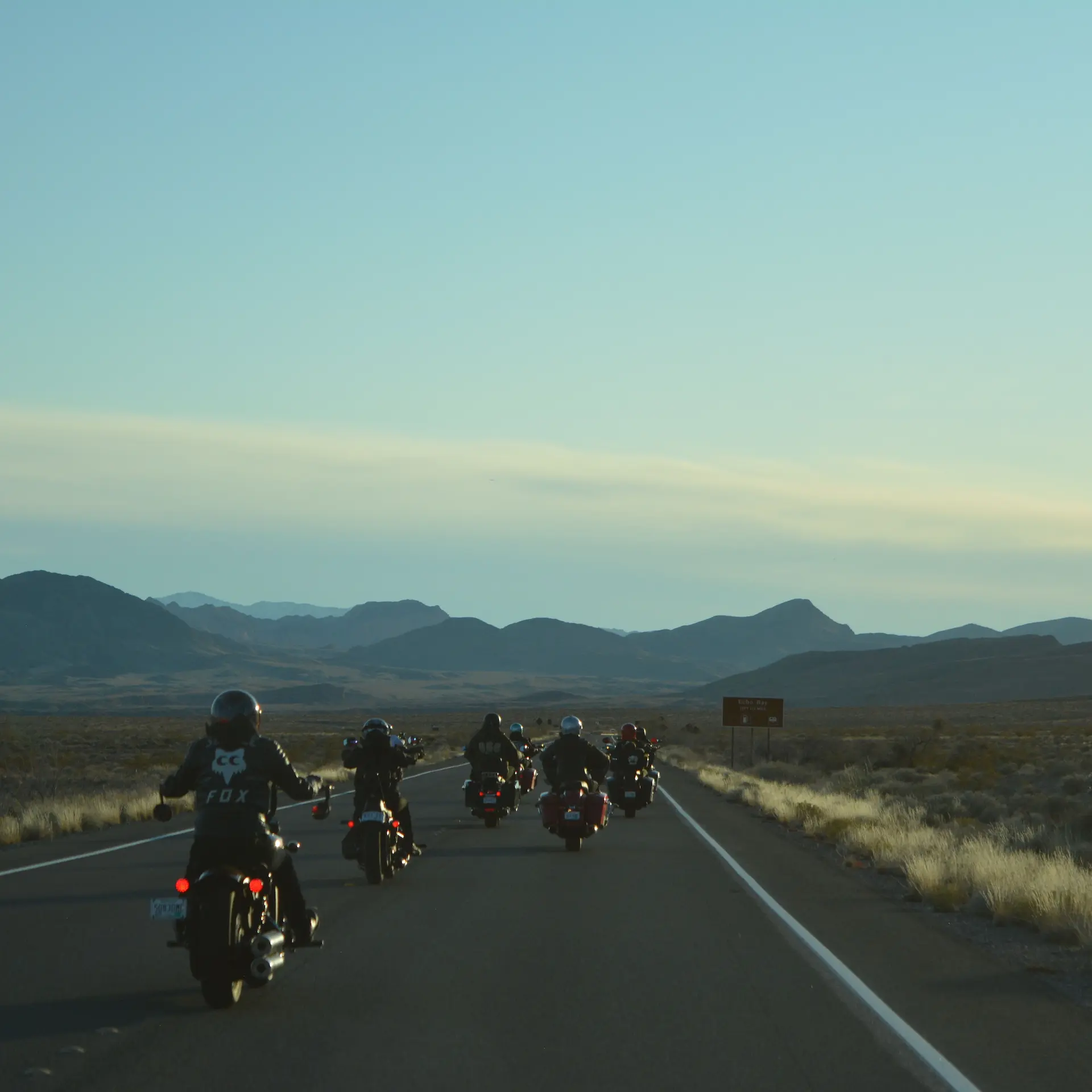 A group of riders on their motorbikes riding away down the highway towards the mountain ranges.