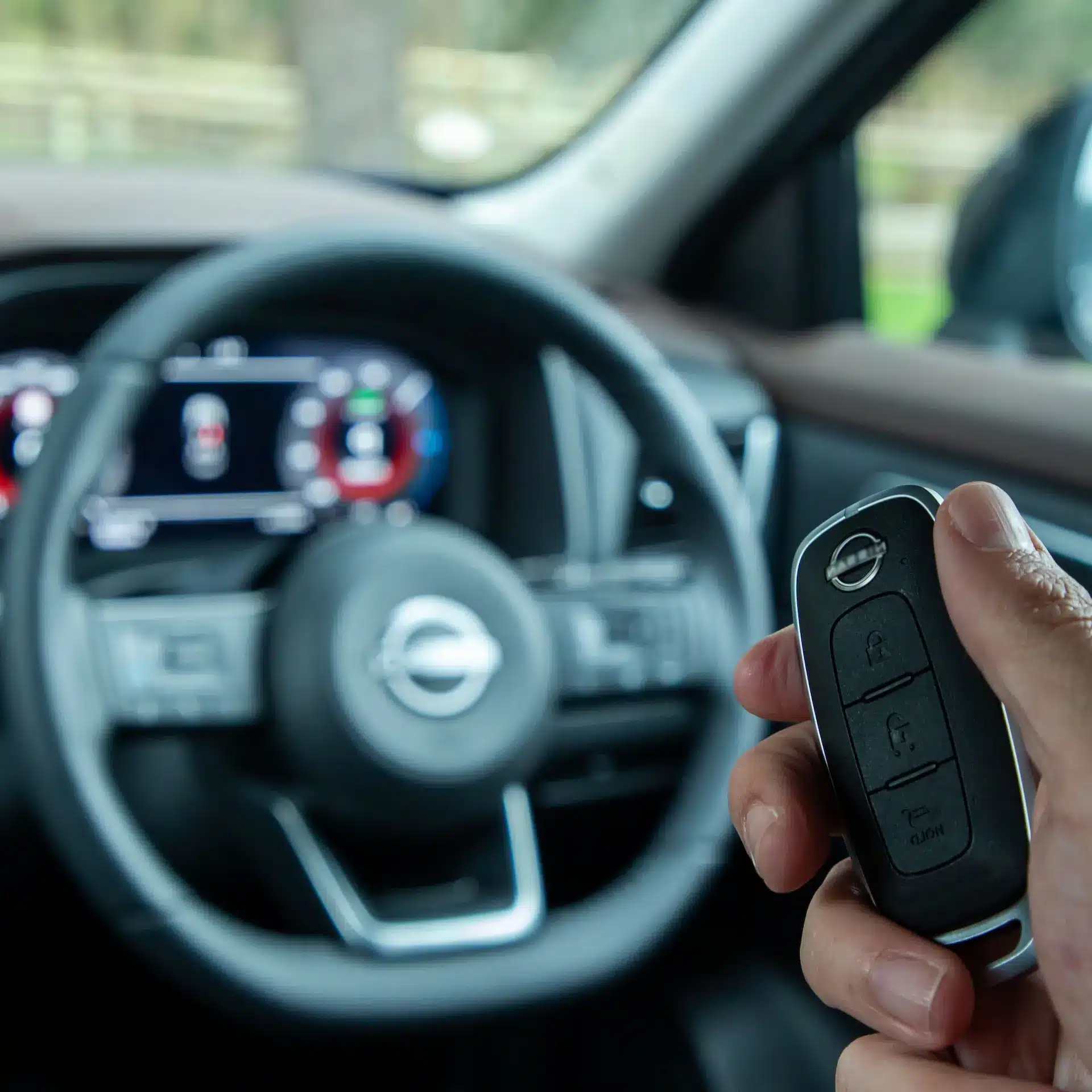 Personal holding Nissan transponder key for a new Nissan model with the interior of the car in the blurred background