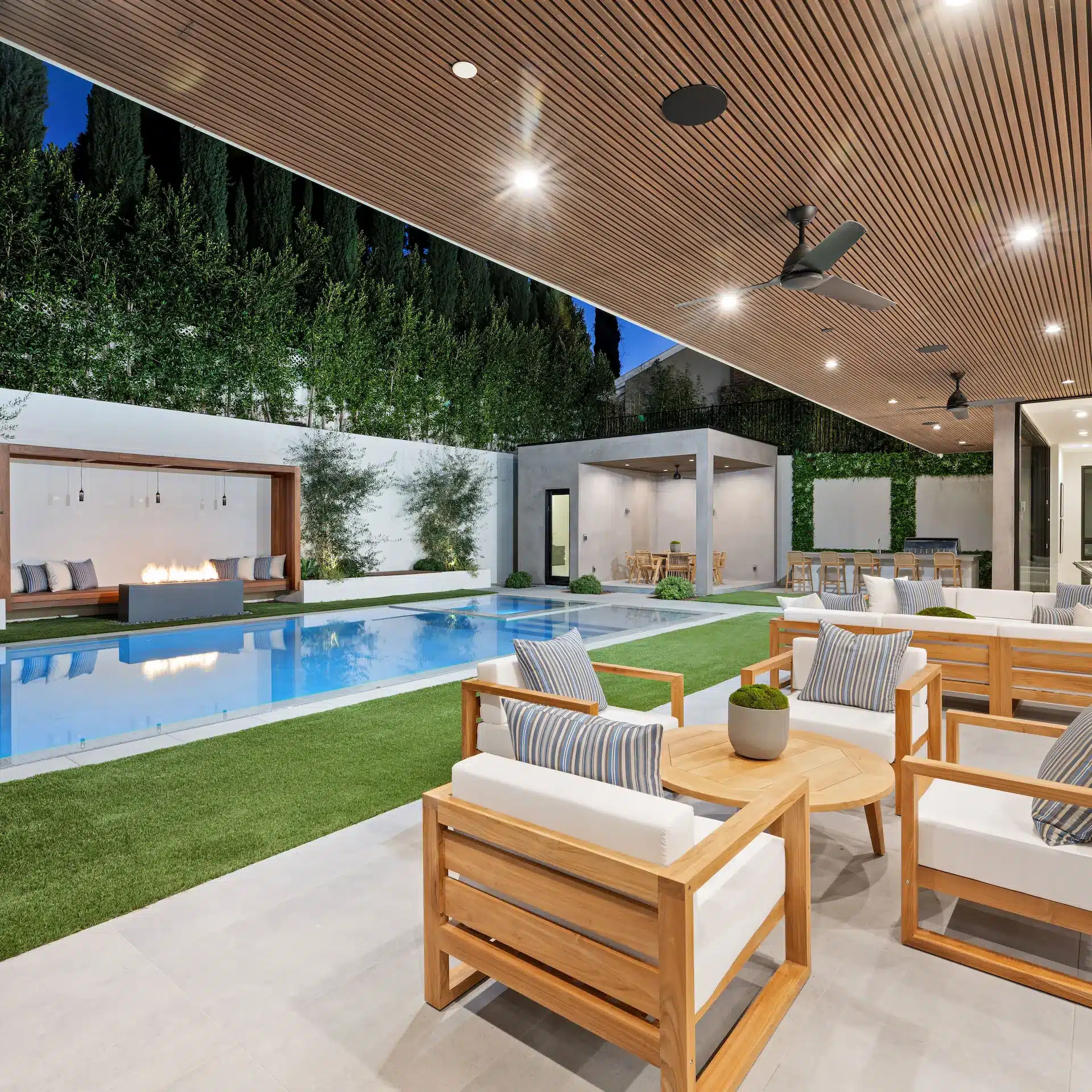 A modern home with a pool nicely lit at early evening with a patio and modern outdoor furniture.
