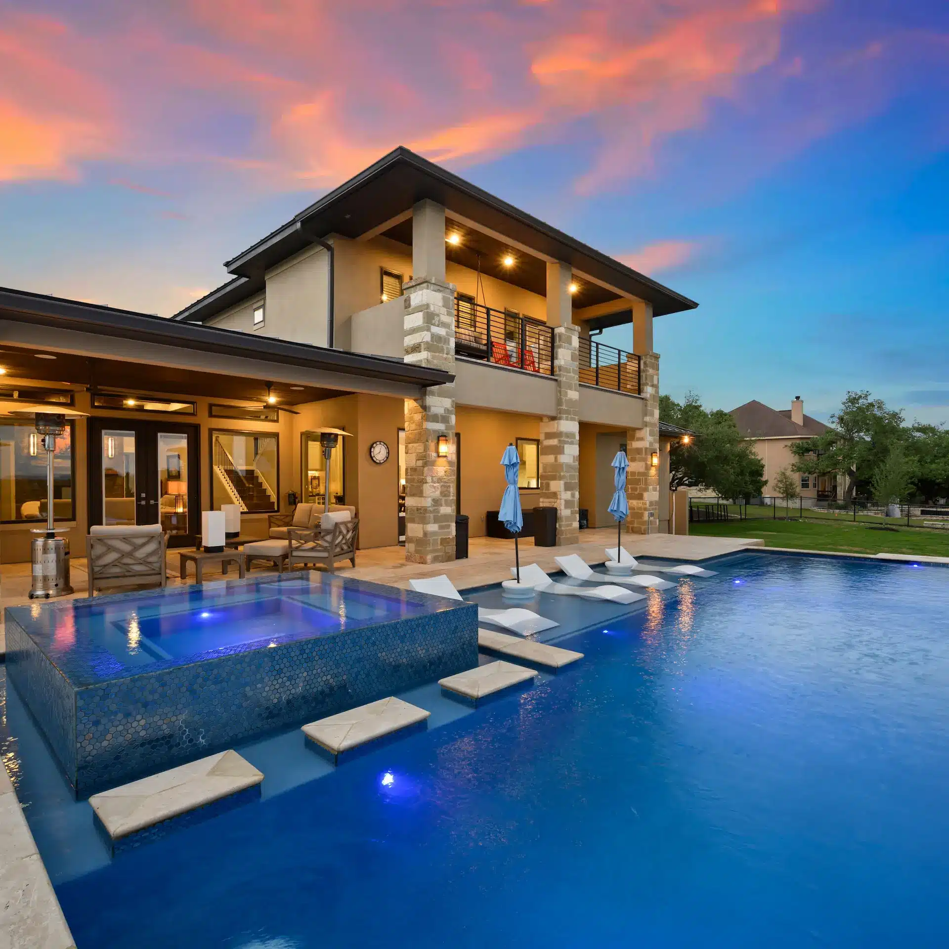 A modern 2 level home with a expansive pool nicely lit at dusk.