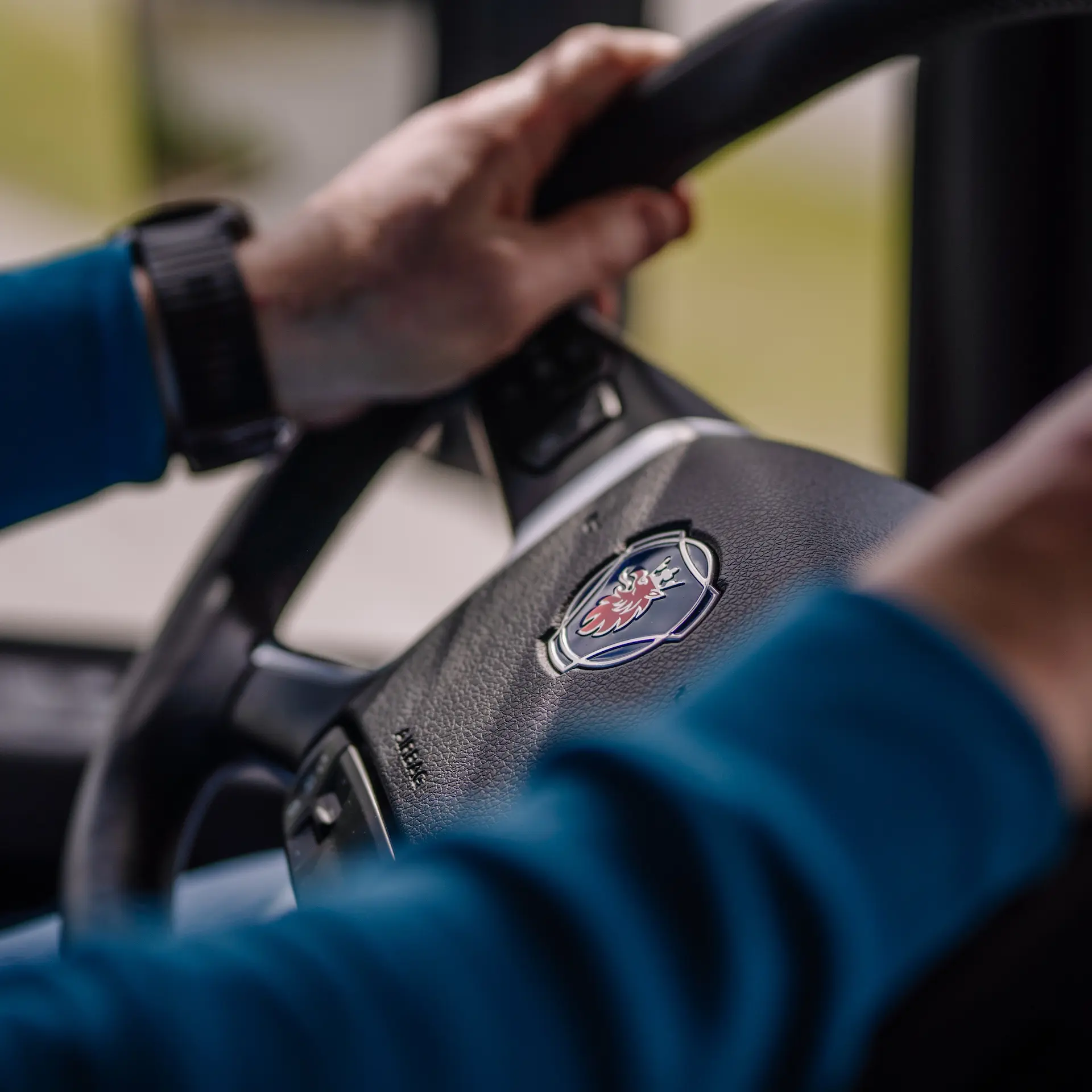 Close up view of steering wheel in the cab of a Scania truck while being driven with the drivers hands on the wheel.