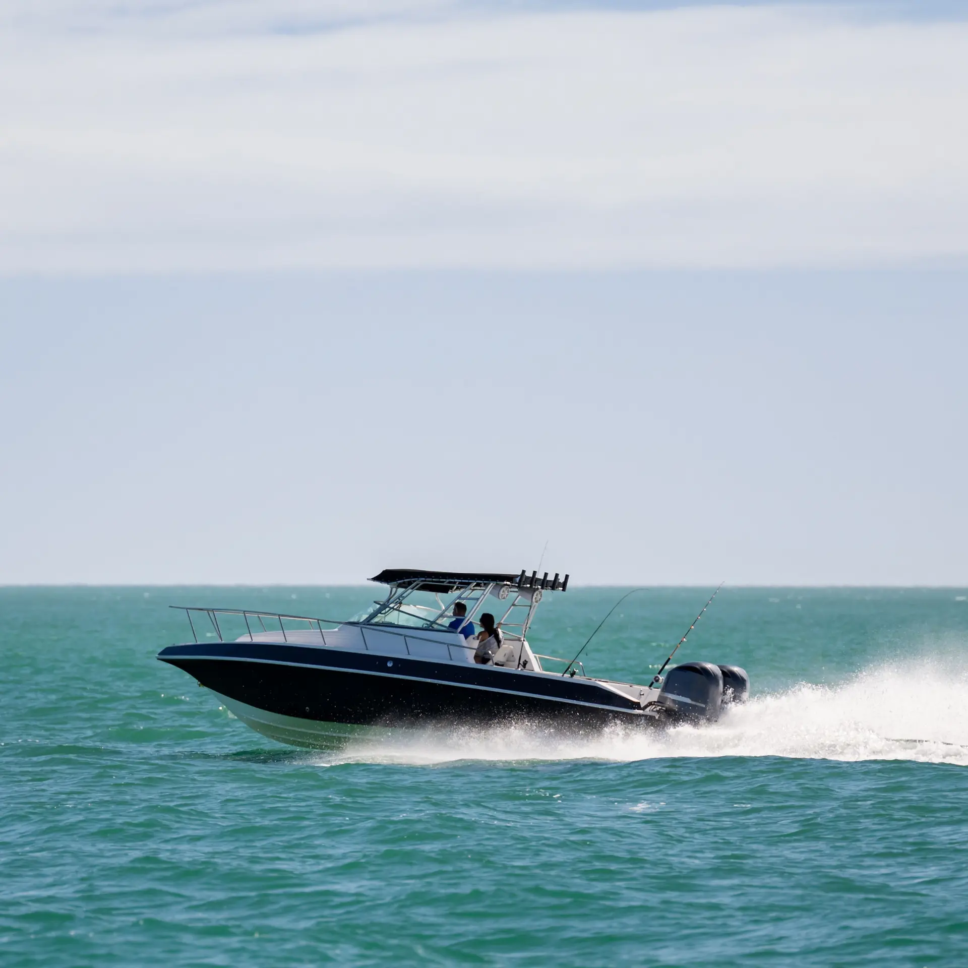 A boat speeding across calm waters making lots of spray on a bright sunny day.