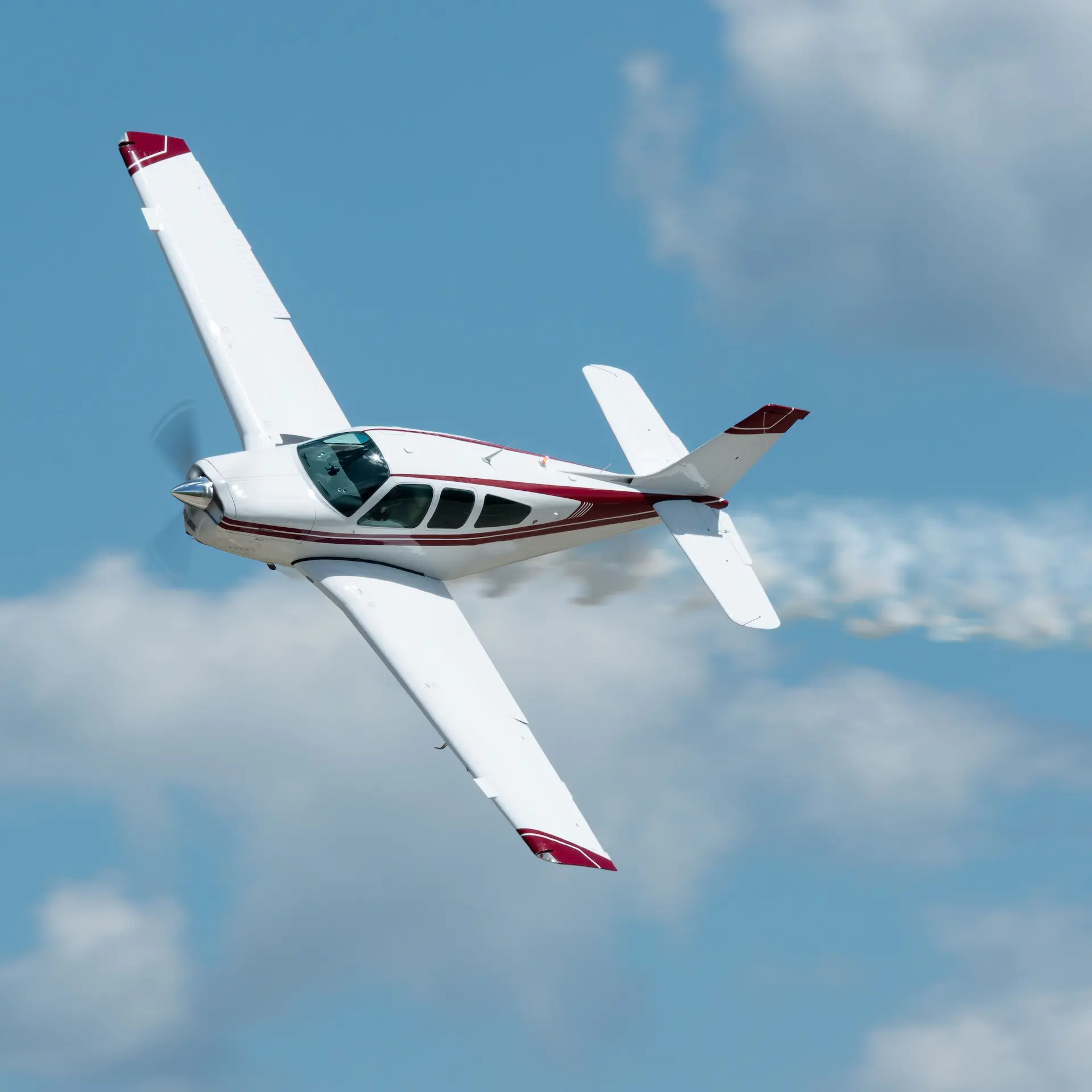Small plane flying through clear skies leaving a trail behind