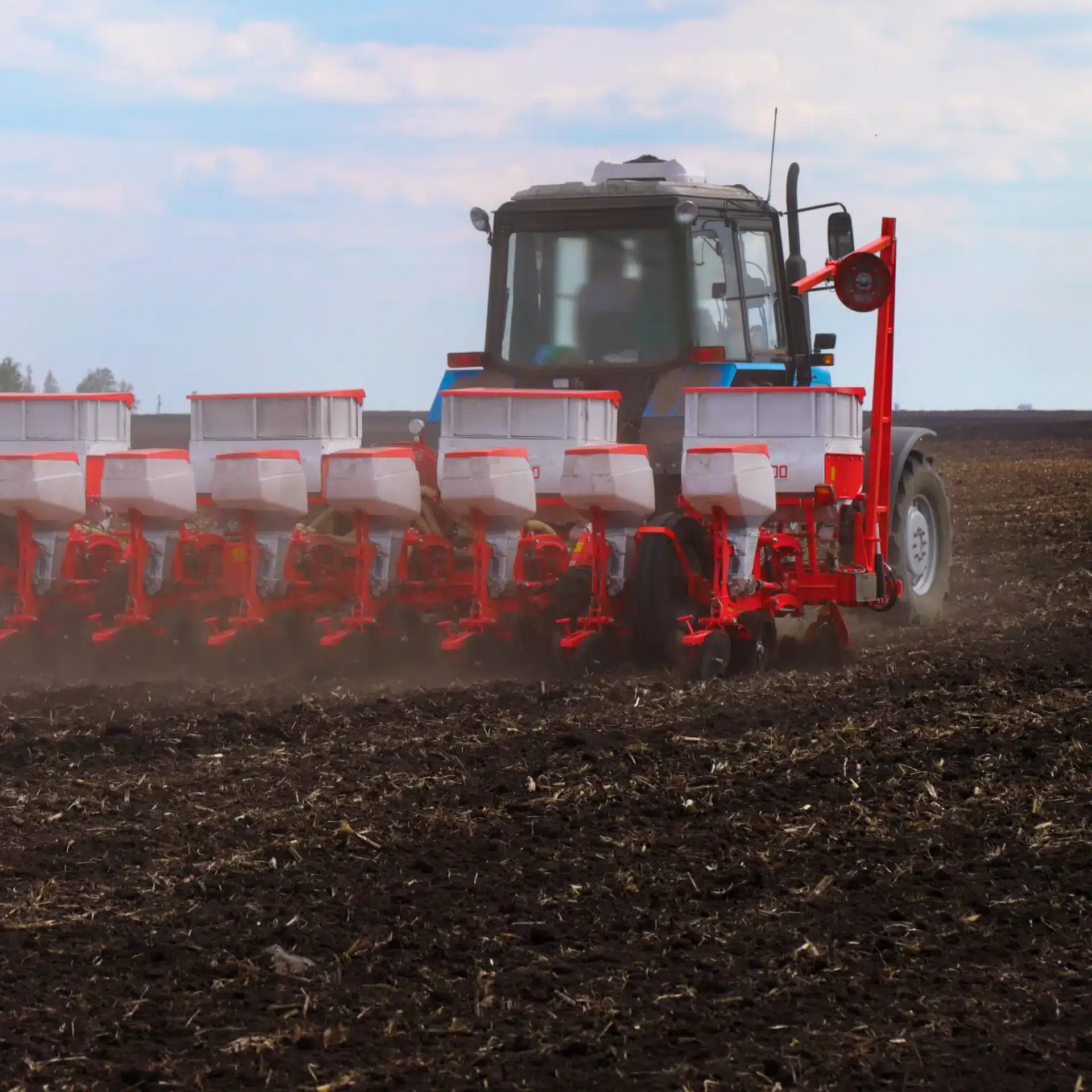 A seeder attached to a tractor is planting seed in a field.