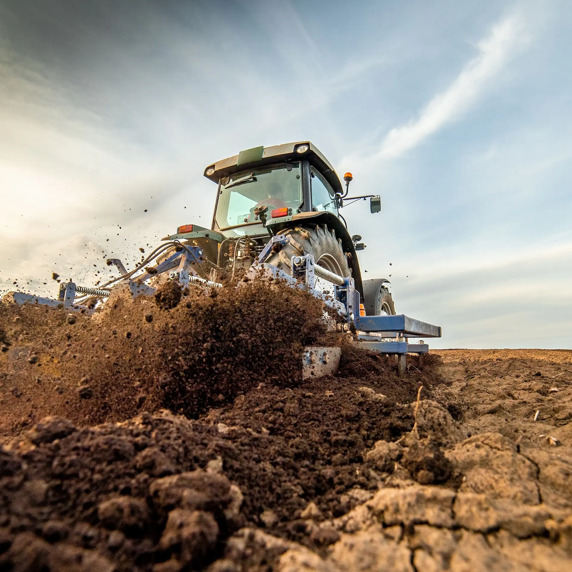 A tillage attachment on a Tractor ploughing up the soil in a field being prepared for seeding.