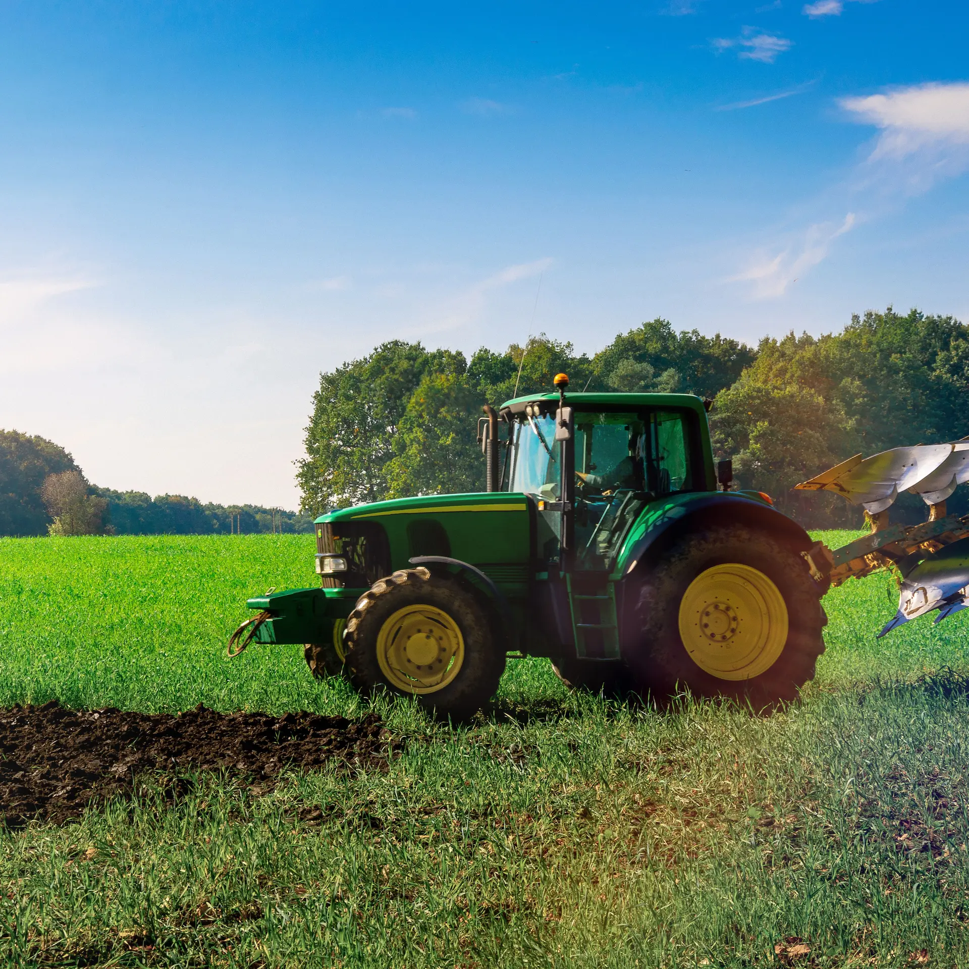 A John Deere tractor with a ploughing attachment working in a field on a bright sunny day.