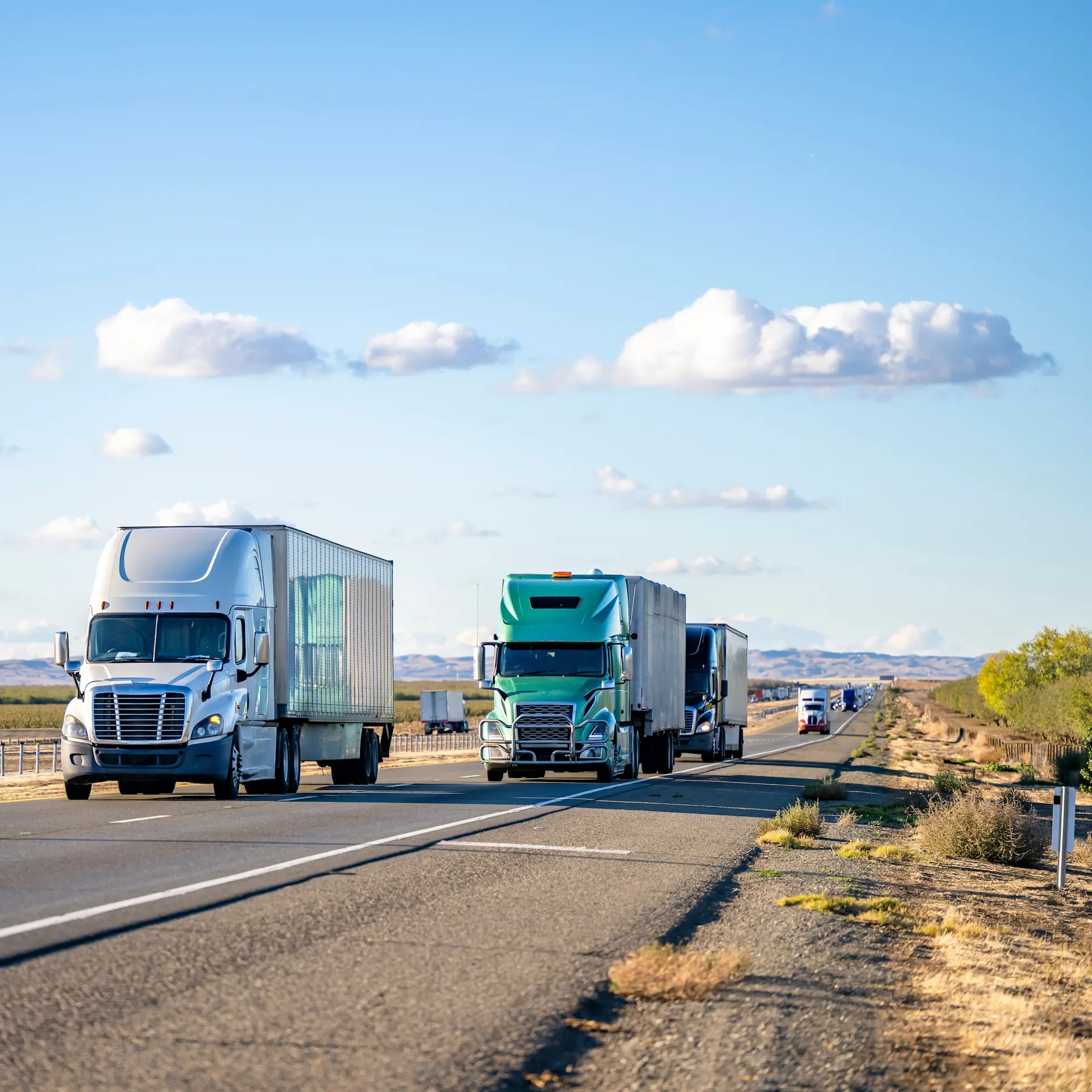Several trucks driving down the highway on a sunny day.