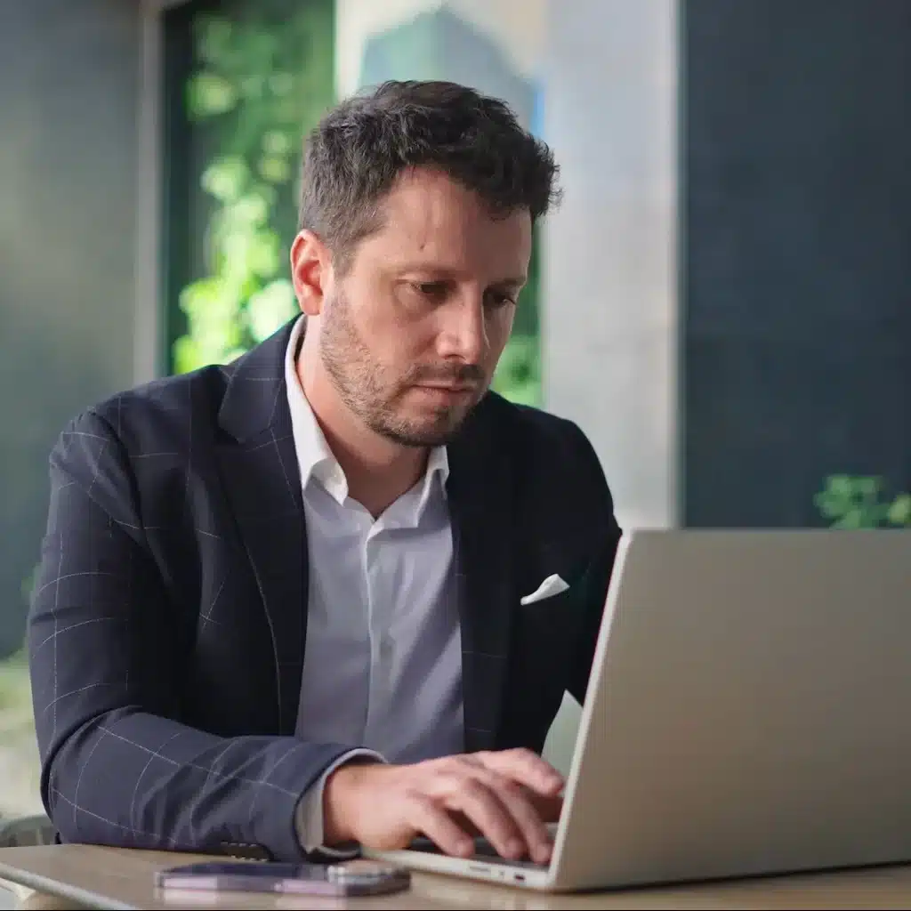 A business man in Brisbane is sitting at a table in an outdoor space using his laptop to learn more about his commercia finance options.