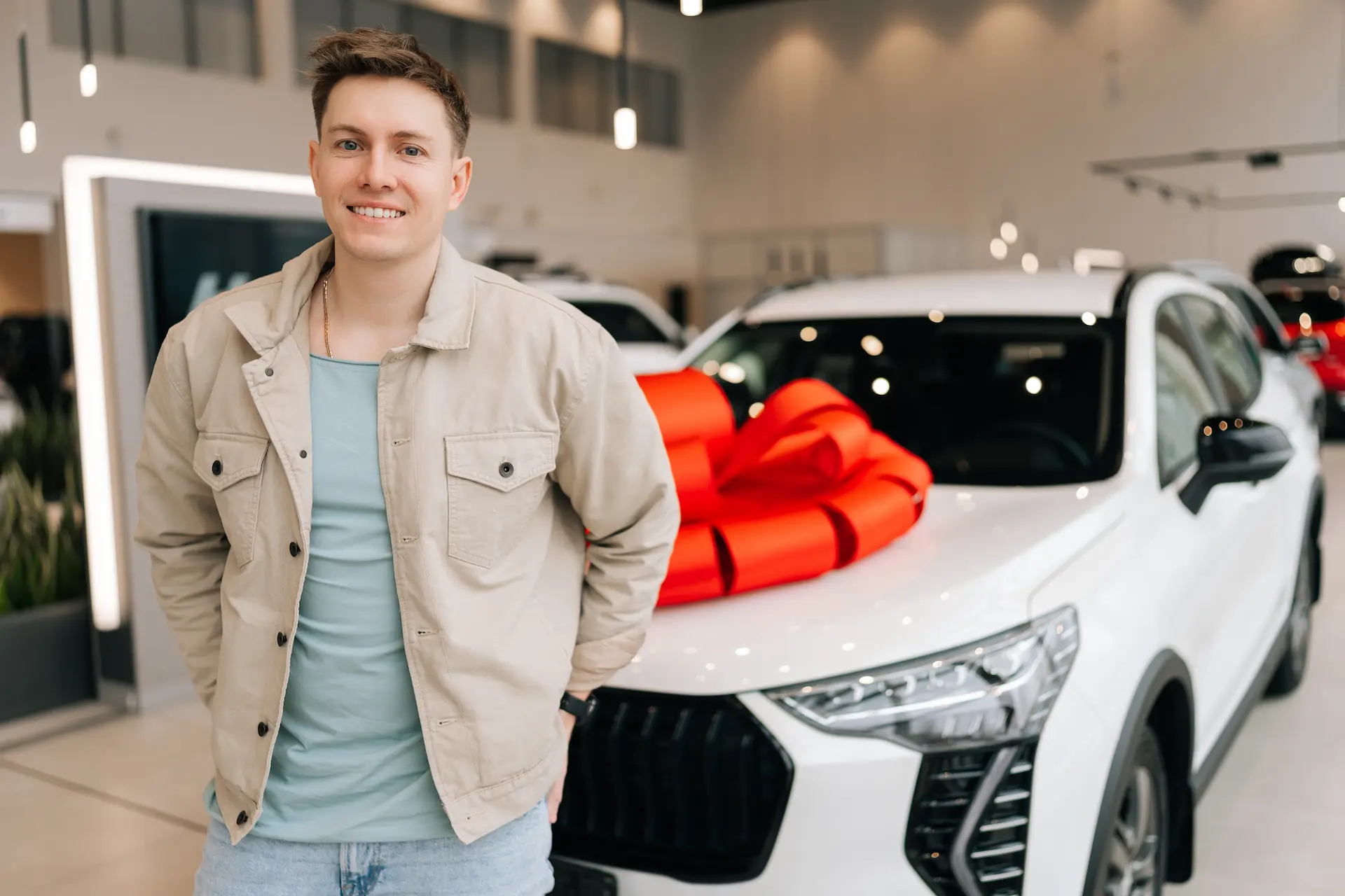 A man standing in front of his new car at the dealership showroom.