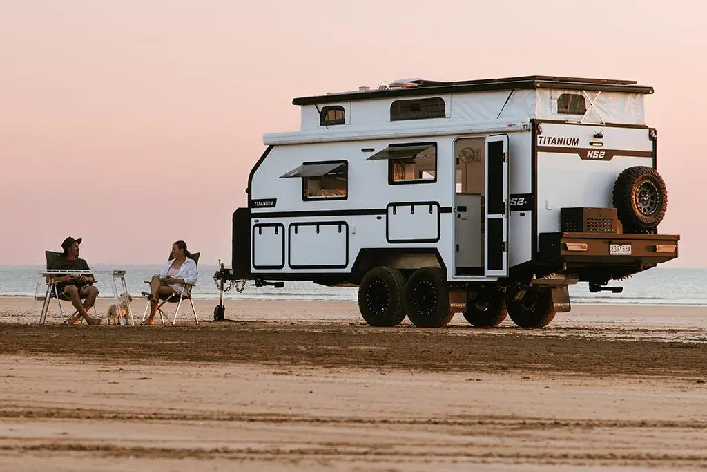 Couple sitting next to their caravan parked on a beach at sunset