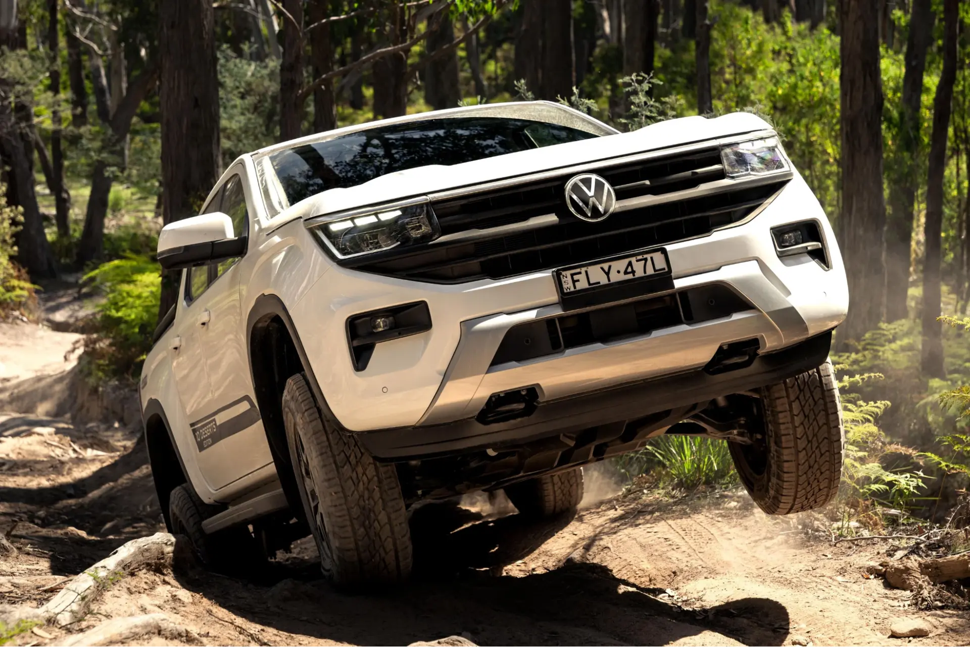 White VW Amarok with a front wheel in the air as it climbs a rutted offroad track