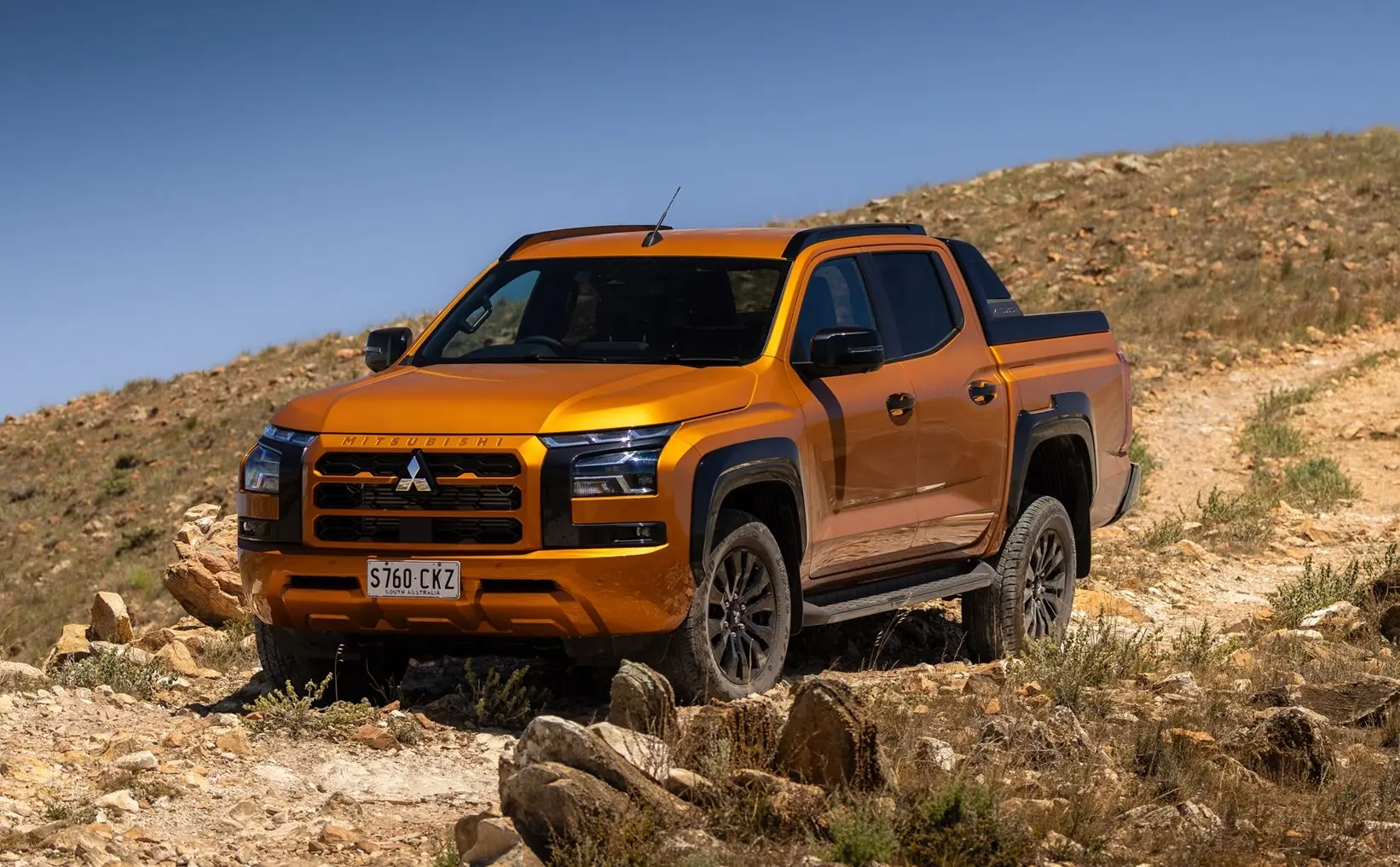 Orange Mitsubishi Triton driving down a dirt track on the site of a hill