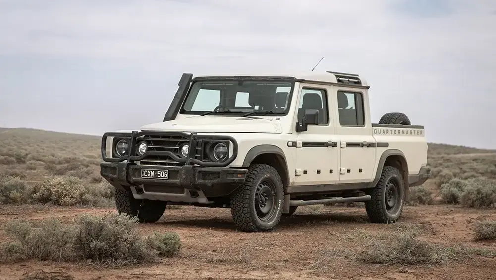 A white INEOS Grenadier Quartermaster parked on a dirt clearing in the outback