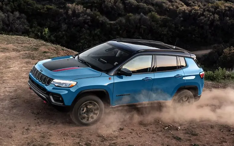 2026 Jeep Compass in blue with black roof driving off-road, kicking up dust.